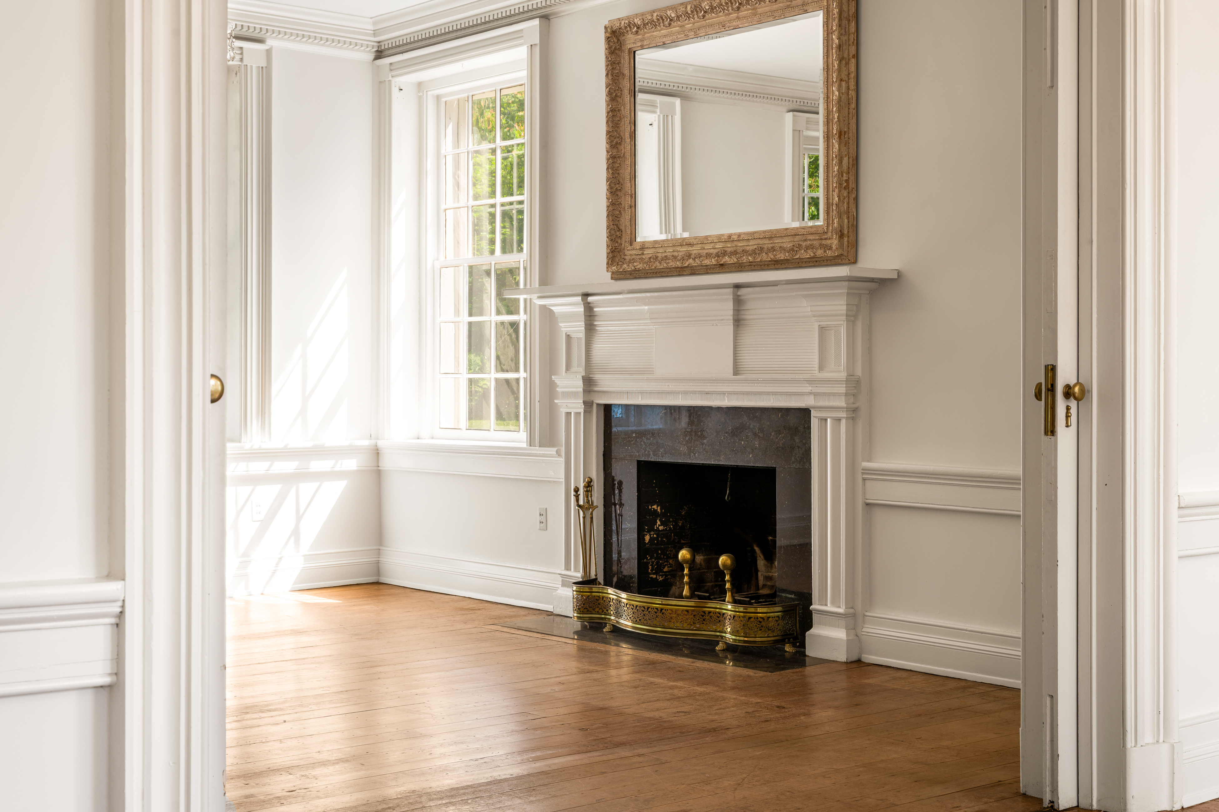 A parlor with fireplace, tall sash windows, and mirror